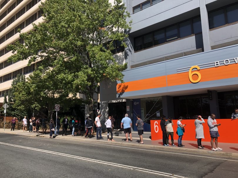 Queue of people on footpath by street waiting for Centrelink in Woden.