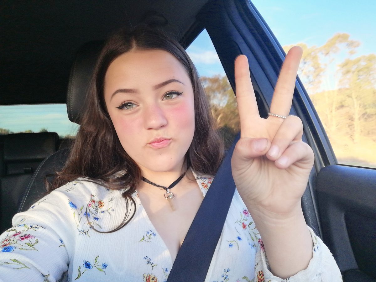 Alexis Saaghy in passenger seat of car making peace sign.