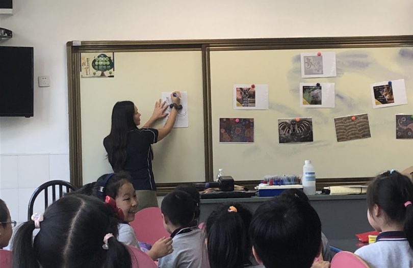 Teacher pinning paper to a board in front of students