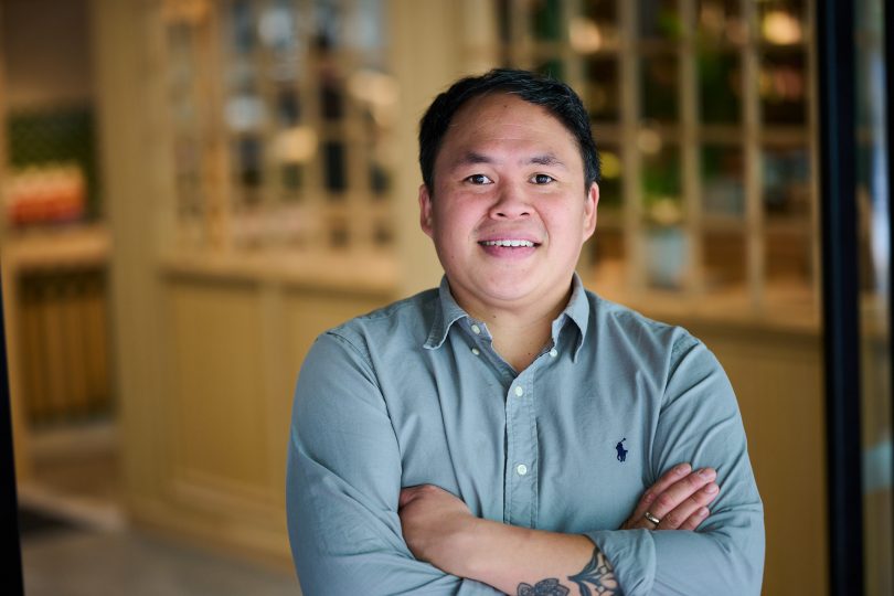 Man in blue shirt smiles for camera with crossed arms.