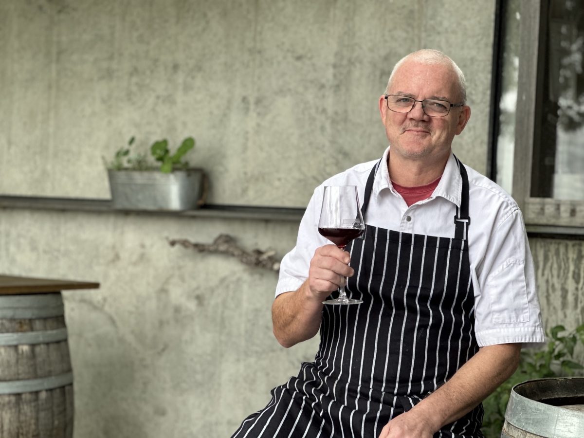 Lerida Estate's Head Chef Tim Crick in his chef's gear, raising a glass of red wine