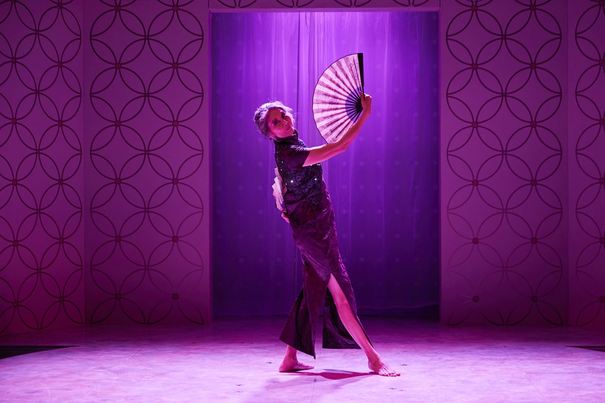 a woman holding a fan on stage bathed in purple light