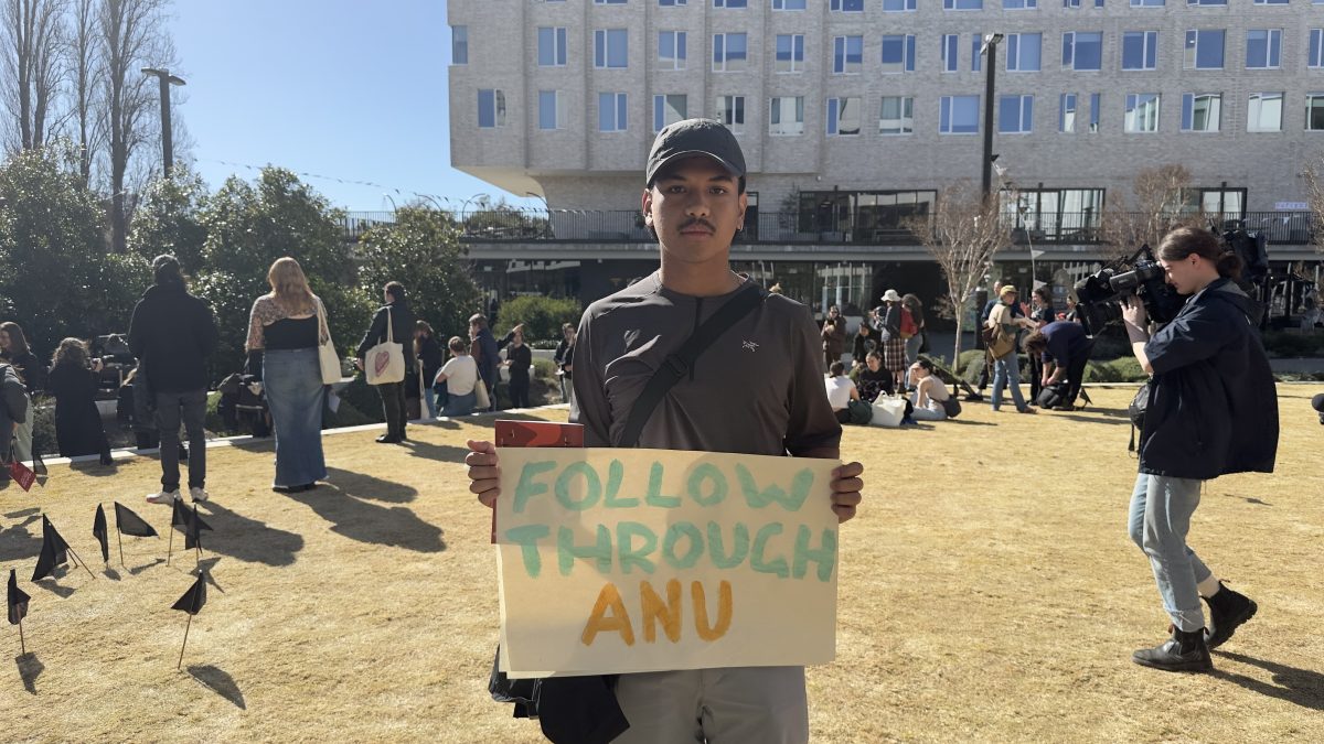 Man holding sign saying 'follow through ANU'
