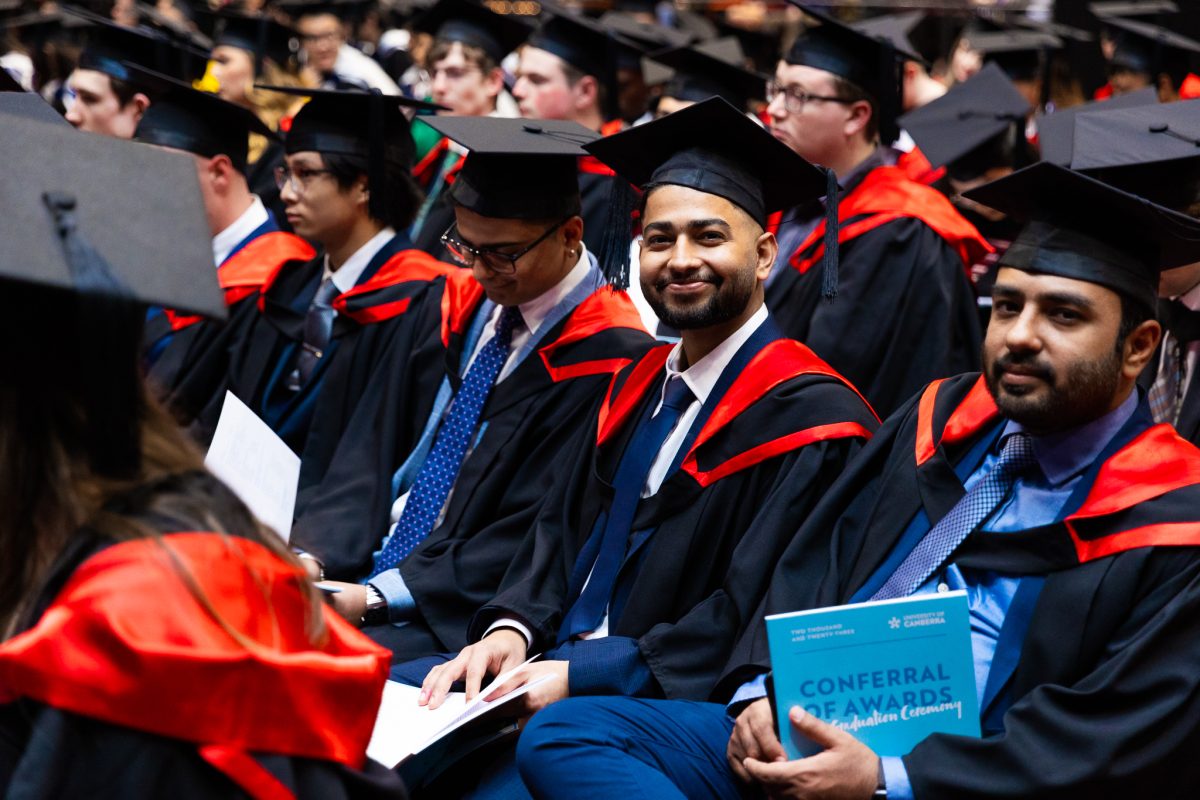 Rows of graduates are pictured, one smiling at the camera, at a University of Canberra graduation ceremony.