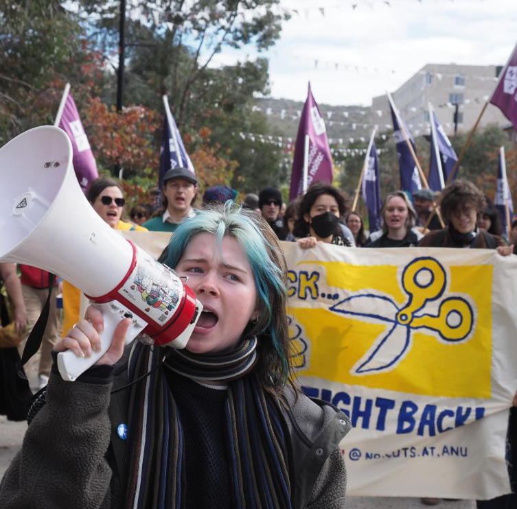 protester holding megaphone in front of 'fight back' sign