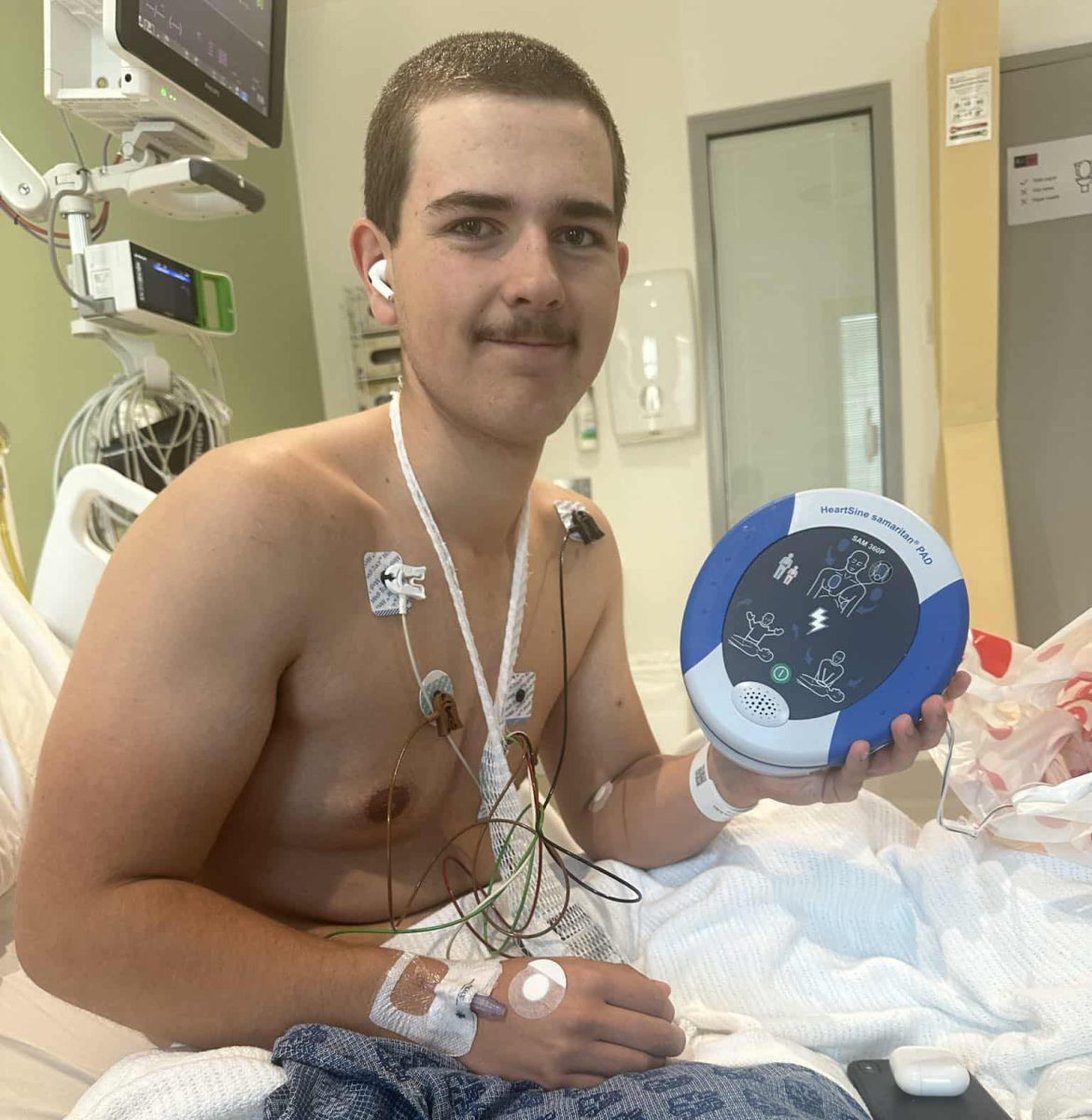 A teenager in a hospital bed holding an AED that was used on him