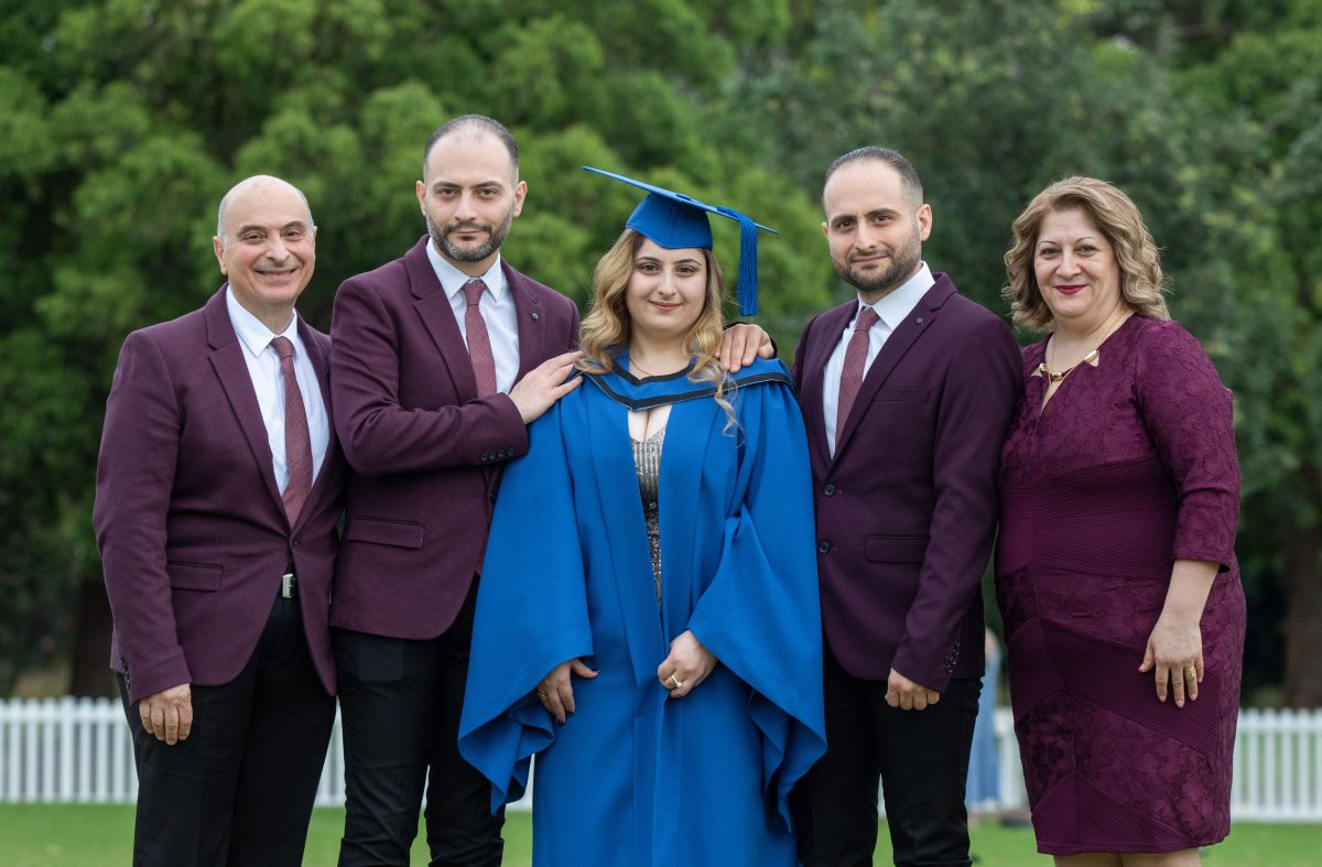 University of Wollongong engineering graduate Lord Thabet in her ceremonial graduation robes and hat, standing with her family